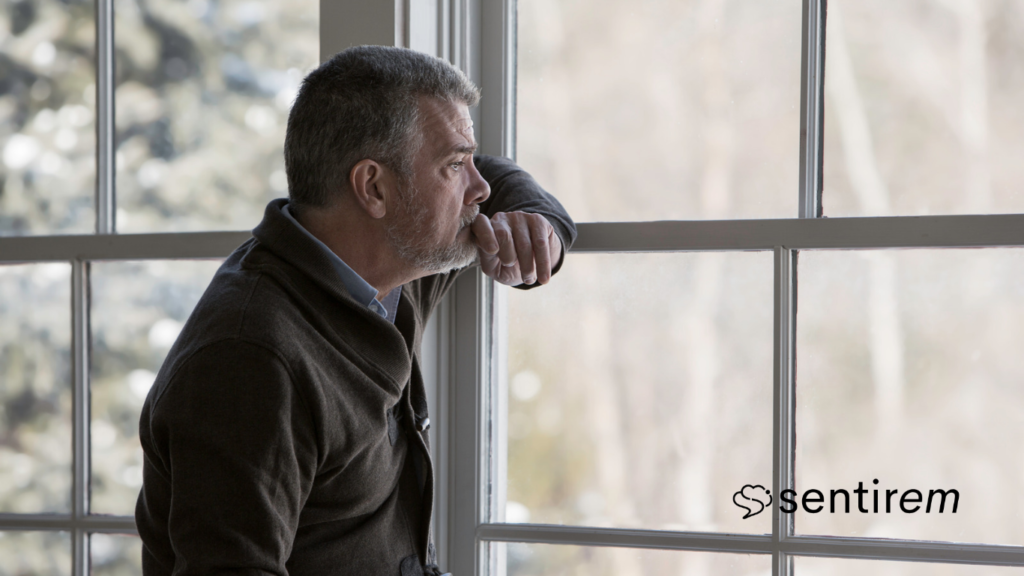 Hombre mayor mirando por la ventana con gesto pensativo, en un momento de duelo y reflexión